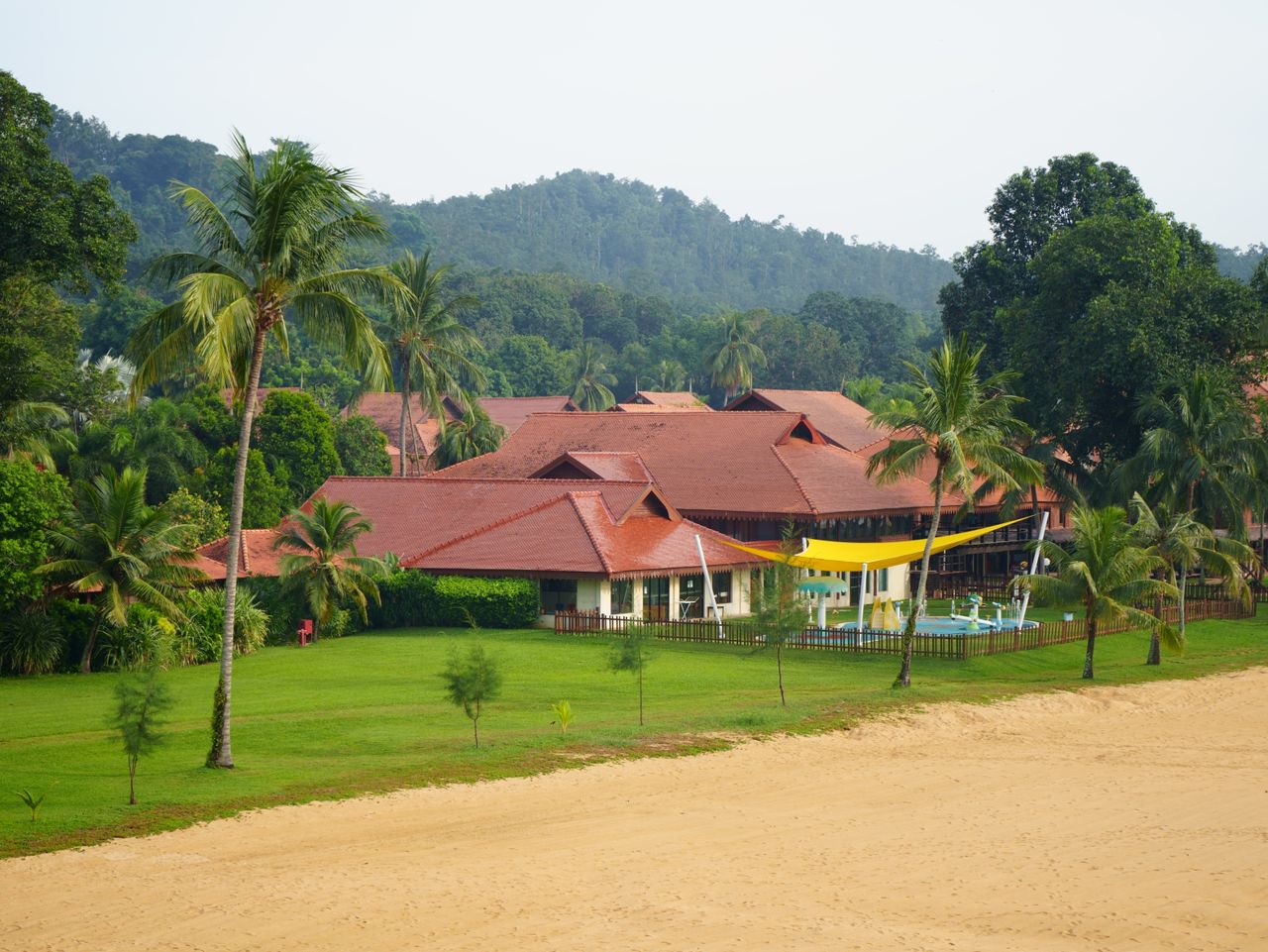 Services Scenic view of a tropical beachfront resort with lush greenery and palm trees.