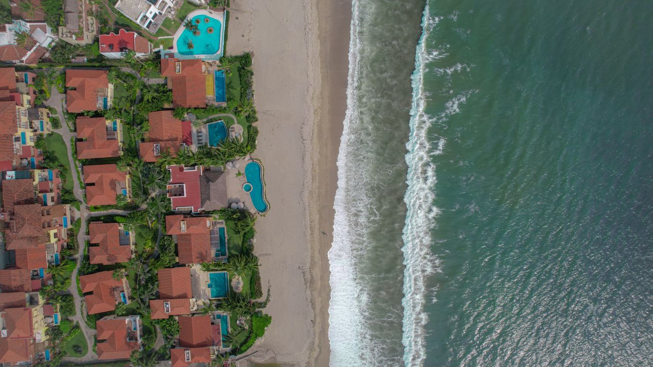 Services Aerial view of beachfront villas with pools and lush greenery along the shoreline.