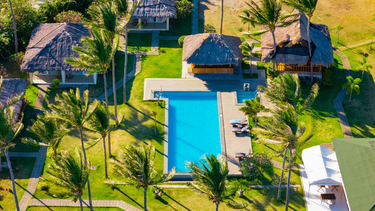 Services Stunning aerial view of a tropical resort with a pool, lush greenery, and palm trees in Bacong, Philippines.