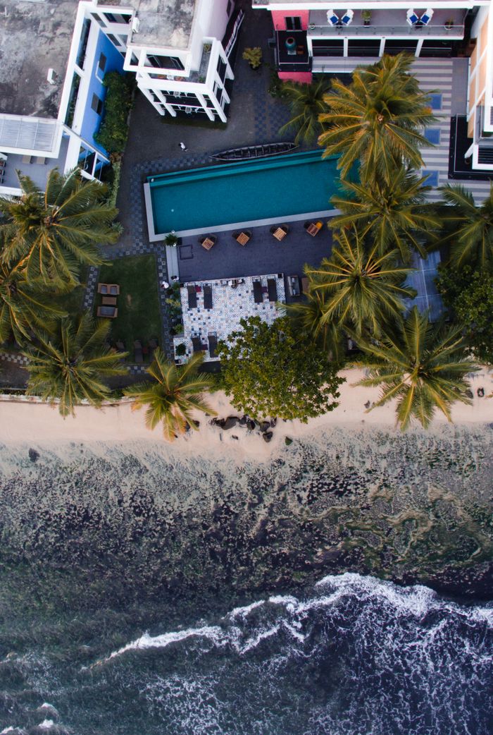 About A breathtaking aerial view of a beachfront resort with palm trees and a pool near the ocean.